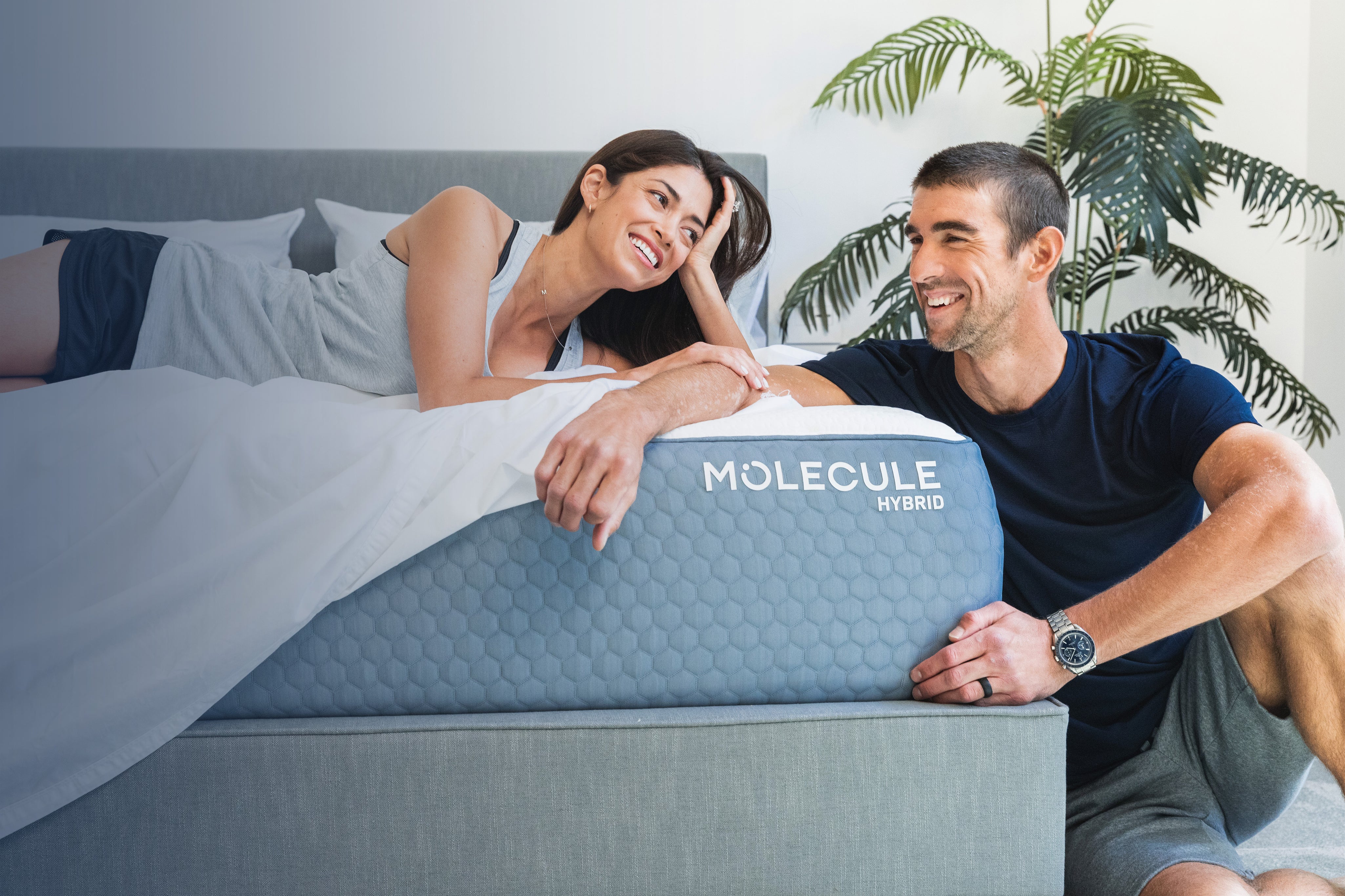 Alex Morgan laying on a Molecule Hybrid Mattress while looking at Michael Phelps who is sitting on the floor looking back at her