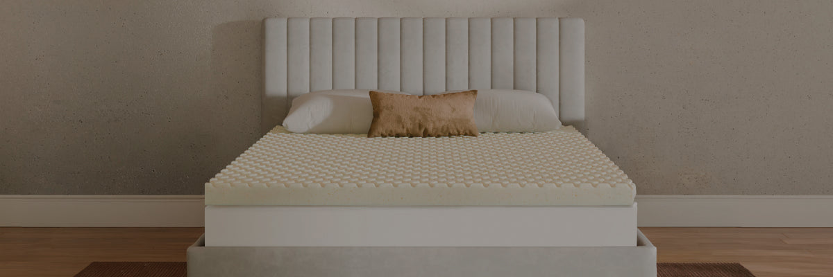 A bed with a textured cream mattress topper and matching pillows, set against a modern white tufted headboard and bed frame, in a minimalist bedroom setting.