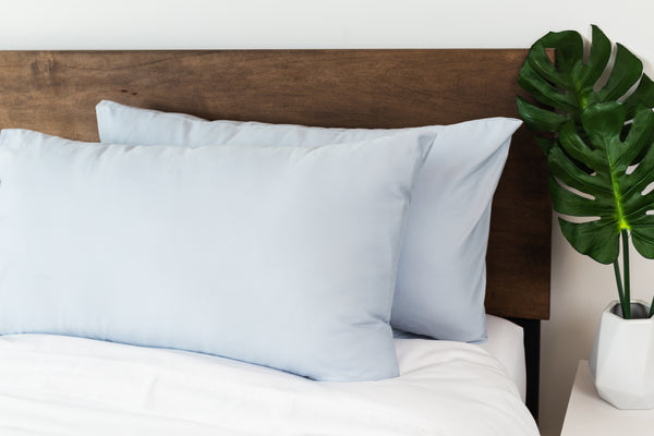 Two light blue MOLECULE pillowcases on a made bed with a wooden headboard
